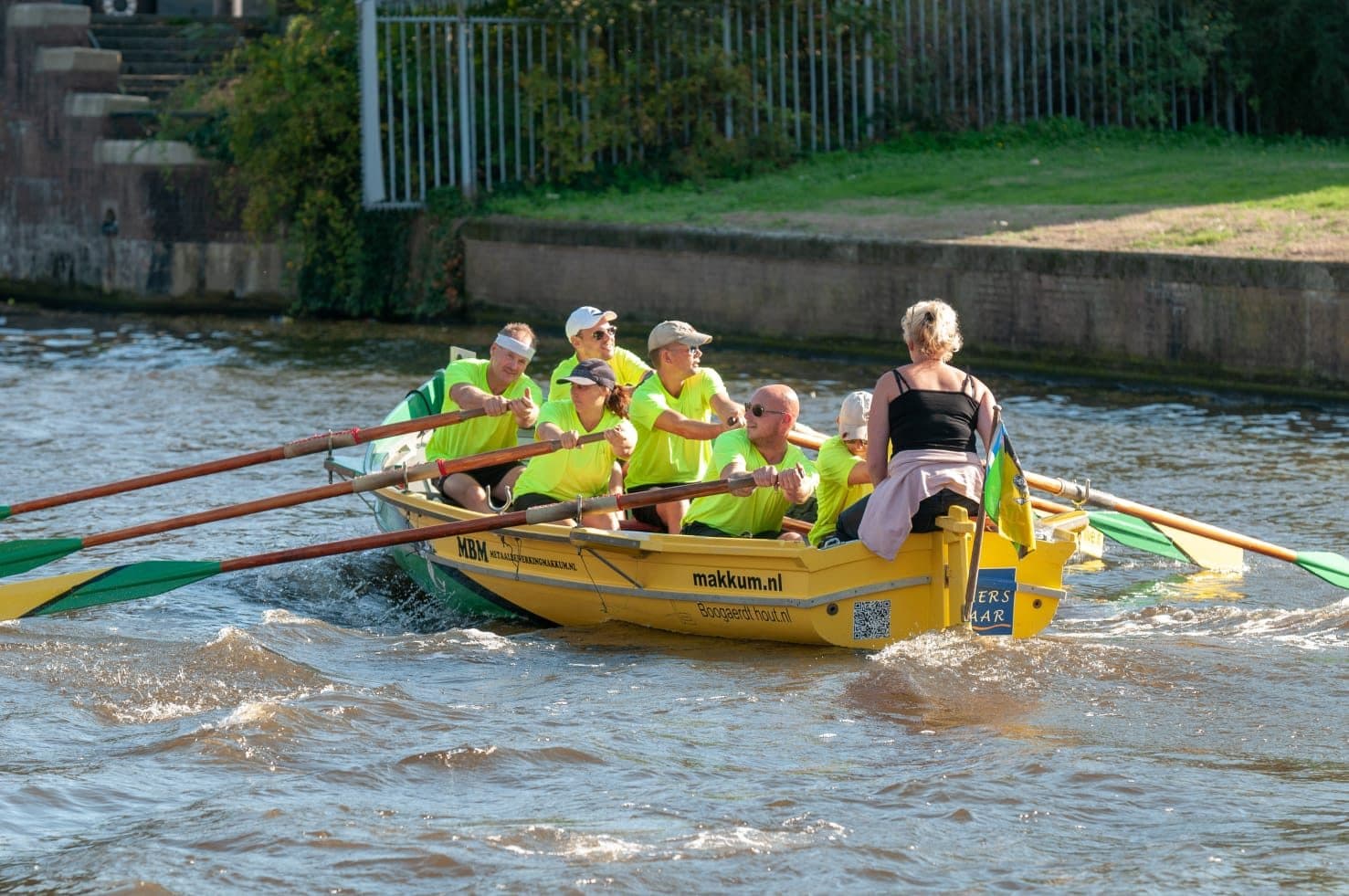Een roeiploeg in een gele roeiboot op het water bij Makkum